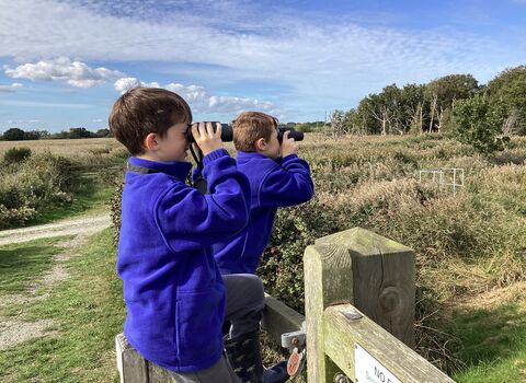 Two primary school children in uniform looking through binoculars at a nature reserve