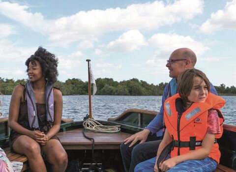 Three people enjoy a boat trip on Ranworth Broad
