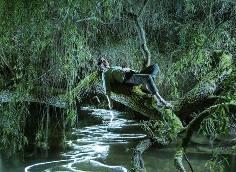 An album cover showing Sam Lee reclining on a horizontal tree branch across a stream with sparkling white patterns on the water