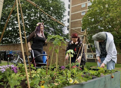 Three local people smiling and gardening together in Mile Cross Norwich